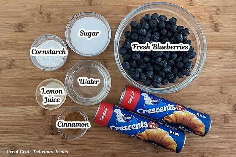 A wood cutting board with all the ingredients needed to make blueberry pie bombs.