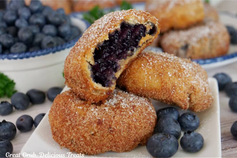 A white square plate with three blueberry pie bombs on it with a bite out of the one on top.