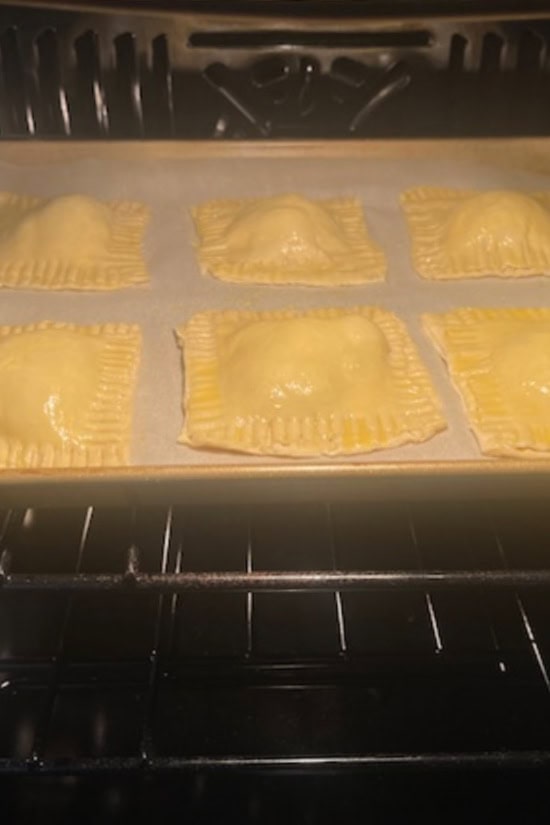 A baking sheet in the oven with blueberry toaster strudels on it baking in the oven.