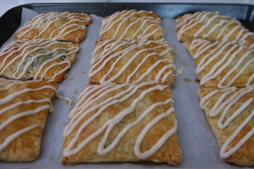 A baking sheet with nine blueberry toaster strudels on it after icing was drizzled over them.