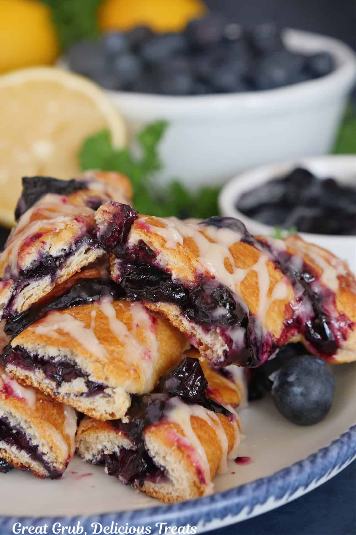 A blueberry twist with a bite taken out placed on a white plate with blue trim with other pastries.