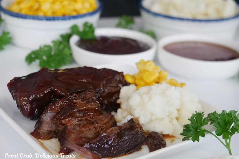 A white plate with beef ribs, mashed potatoes, and corn on it.