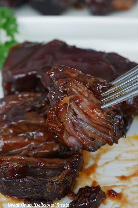 A few boneless beef ribs on a white plate and a bite of rib on a fork.