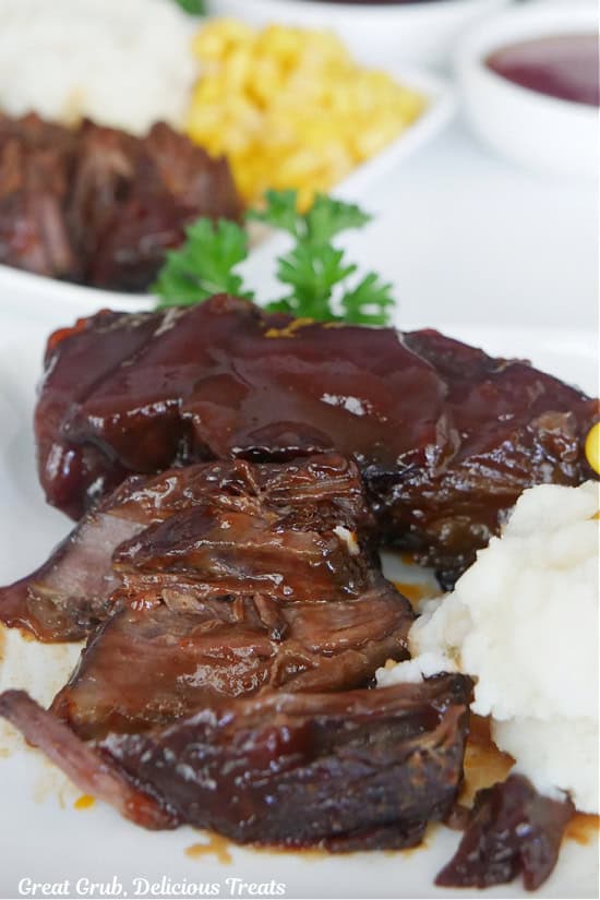 A white plate with boneless BBQ beef ribs, mashed potatoes, and corn on it.