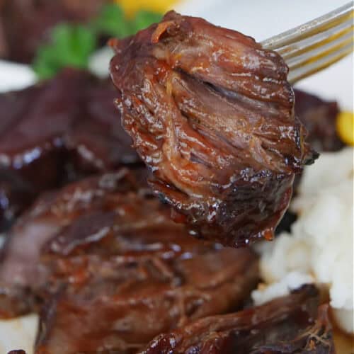 Beef ribs and a bite of the rib on a fork.