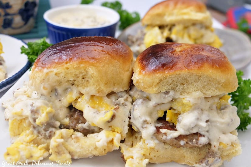 Two sliders sitting side by side on a white plate with a blue bowl filled with gravy in the background.