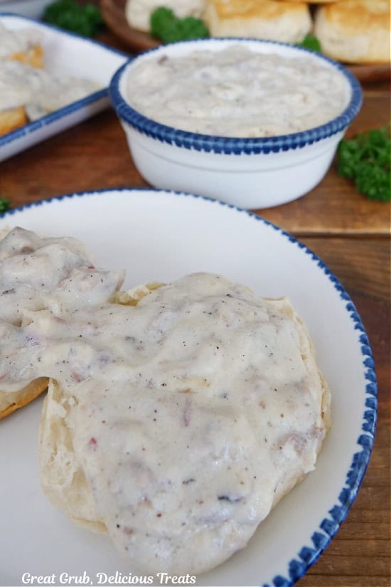 Two biscuits covered with brisket gravy on a white plate with blue trim.