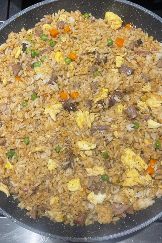 A frying pan with all the ingredients for brisket fried rice mixed together and ready to serve.