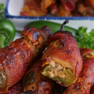 A white plate with blue trim with bacon wrapped jalapeno stuffed with brisket and a cheesy mixture.