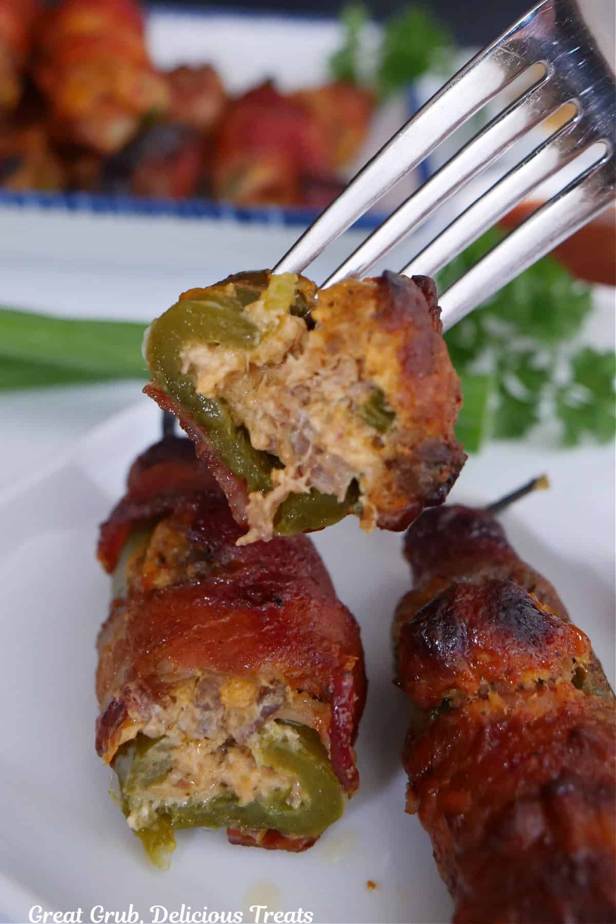 Two stuffed jalapenos on a white plate with a bite of one on a fork.