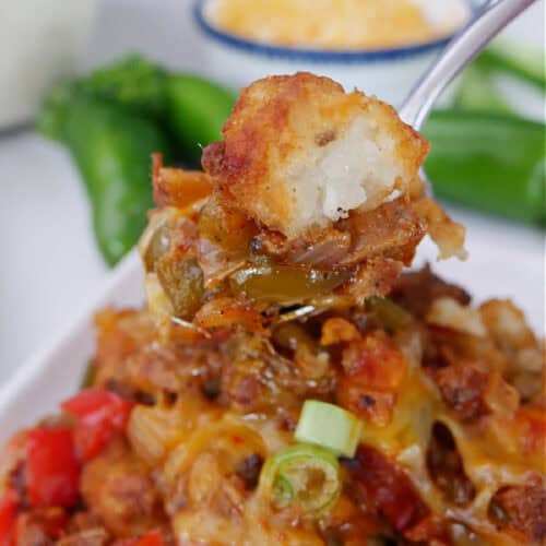 A white plate with a serving of brisket tater tot casserole on it with a bite on a fork.