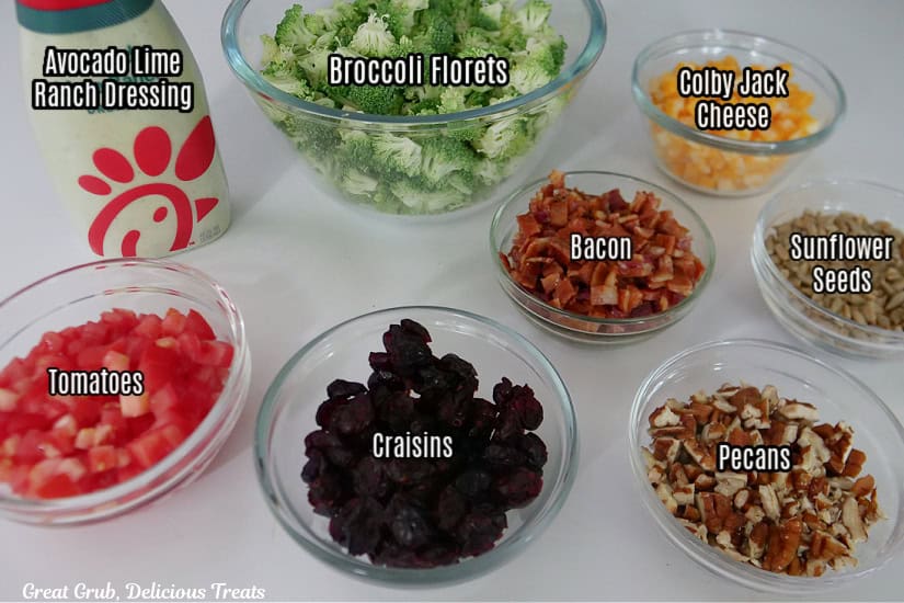 A white surface with all of the ingredients for this salad labeled and in clear bowls.