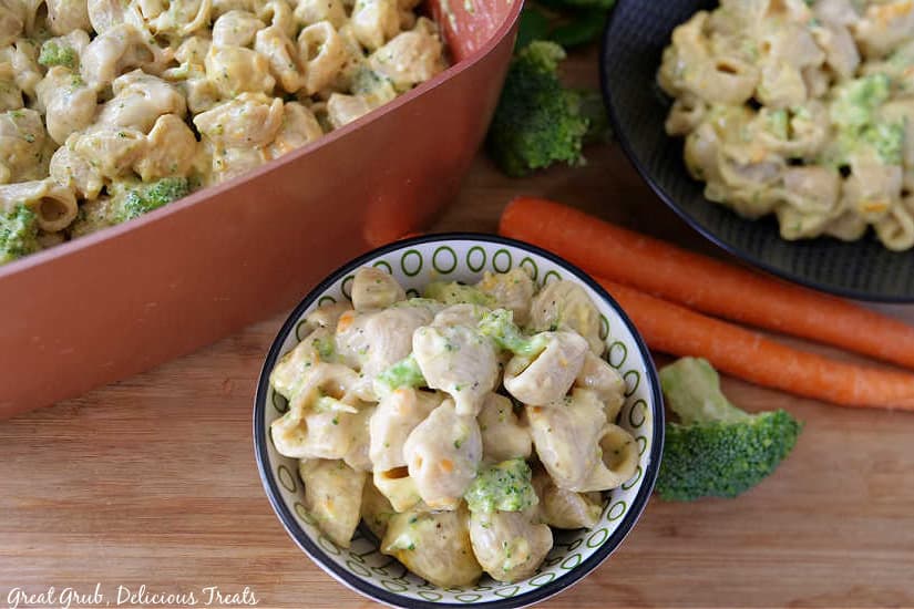 Broccoli Cheddar Mac and Cheese is a deliciously creamy mac and cheese that is loaded with broccoli and shredded carrots. An overhead photo of a pot of macaroni and cheese, a black bowl and a white bowl filled with mac and cheese, with carrots and broccoli florets in the background for decoration.