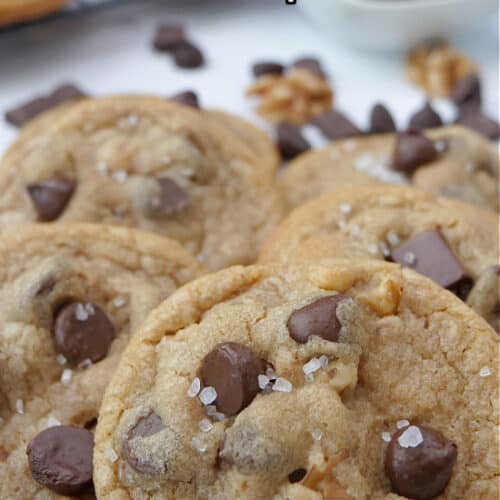 A white surface with chocolate chip cookies on it with more in the background.