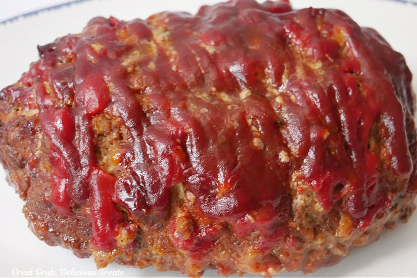 A white plate with a whole meatloaf on it before it is sliced.