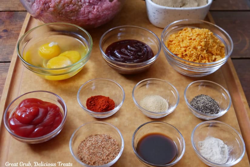 A tan cutting board with glass bowls frilled with the ingredients for brown sugar meatloaf.