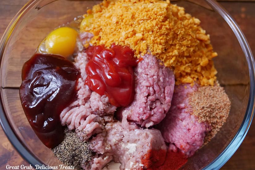 A big glass mixing bowl filled with all the ingredients to make meatloaf before it is all combined.