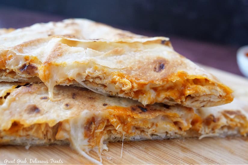 Two sections of a buffalo chicken quesadilla on a wood cutting board showing all the cheese and shredded chicken.