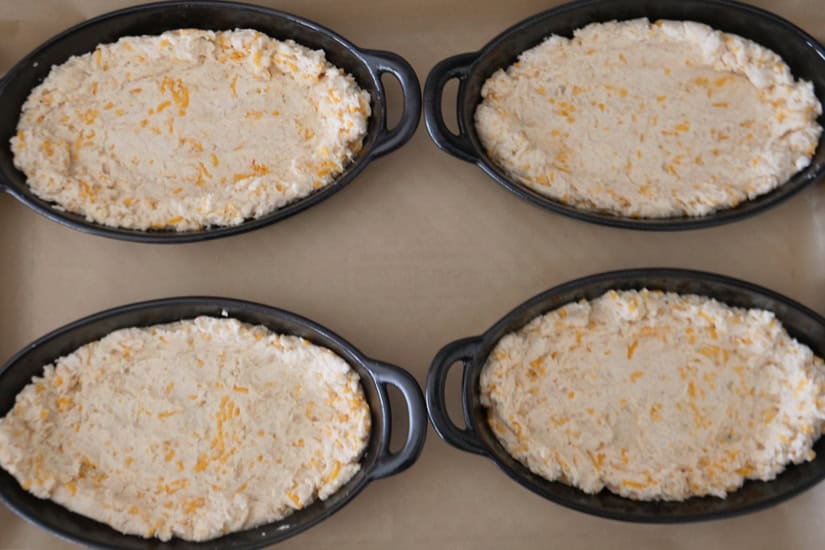 Four oval black baking dishes with the biscuit mixture laid in the bottom and going up the sides.
