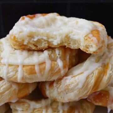 A stack of cheese Danishes on top of each other with a bite taken out of the top pastry.