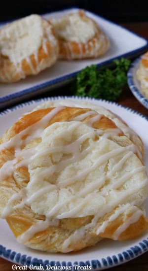 A white plate with blue trim with a cheese danish on it with more danishes in the background.