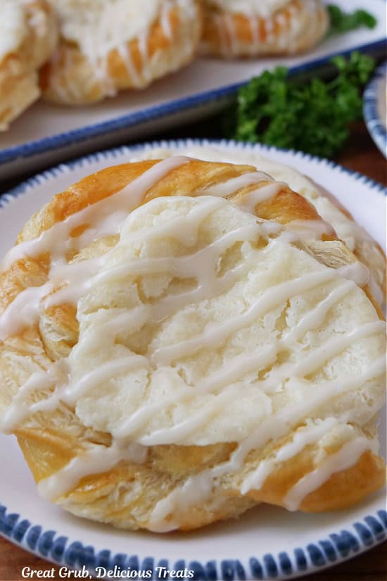 A close up of a cheese danish on a white plate with blue trim.