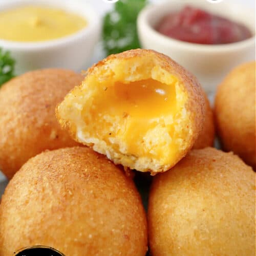 Cheese bites stacked up on a silver tray with a bite taken out of one, showing melted cheddar cheese in the middle.