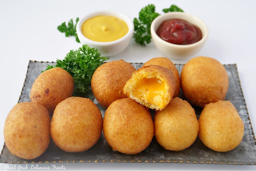 Cheese Bites are crispy and golden brown on the outside, with melted and gooey American cheese in the middle. An oblong silver plate with ten cheese bites on it.