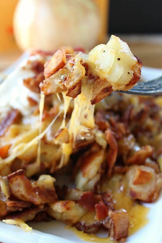 A white plate with fried breakfast potatoes on it and a forkful of cheesy potatoes on it.