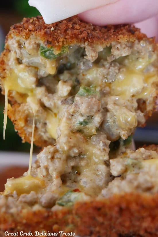 A cheesy ground beef ball being broken in half to show all the melty cheese.