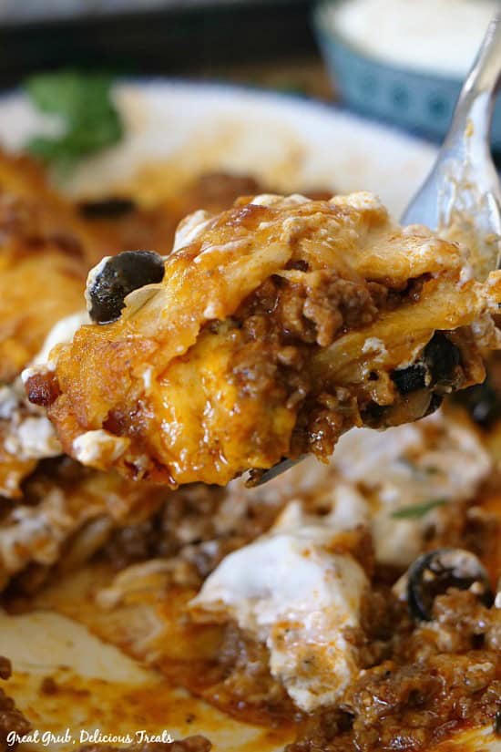 Cheesy Ground Beef Enchiladas are loaded with cheese, are full of seasoned ground beef and rolled in flour tortillas. A bite of beef enchilada on a fork held above the plate of enchiladas.
