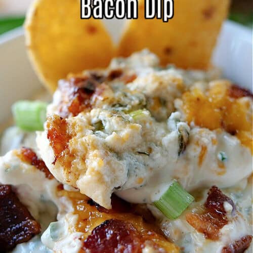 A close up of a serving of cheesy jalapeno bacon dip in a white bowl with two corn chips dipped into the dip.