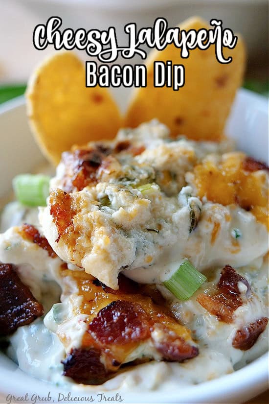 A close up of a serving of cheesy jalapeno bacon dip in a white bowl with two corn chips dipped into the dip.
