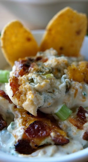 Cheesy Jalapeño Bacon Dip A serving of dip in a white bowl with corn chips in the background.