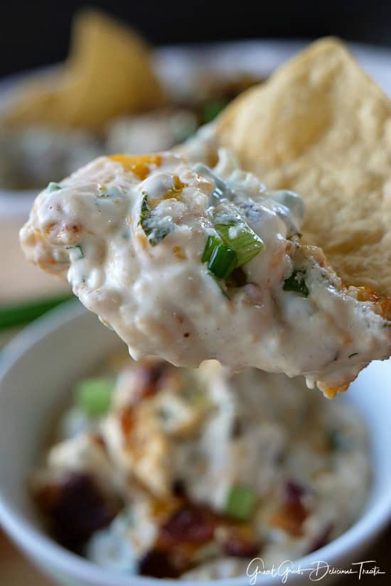 Cheesy Jalapeño Bacon Dip A close up of a tortilla chip with cheesy jalapeno bacon dip on it.