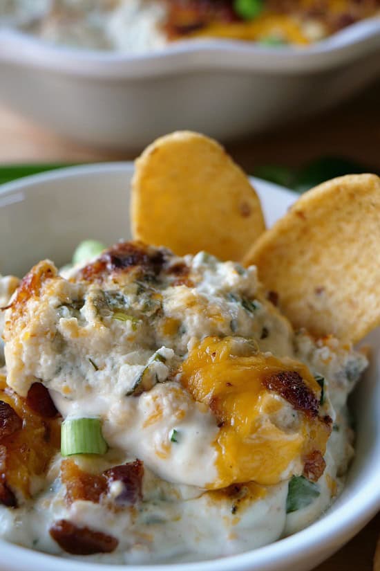 A close up of a white bowl with a serving of dip in it with two corn chips in the bowl.