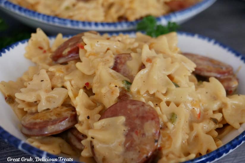 A white oval bowl with blue trim filled with smoked sausage, lots of cheese, and bow tie pasta noodles.