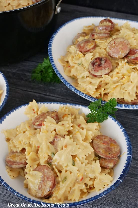 Two white bowls with blue trim filled with a serving of sliced kielbasa sausage and bow tie pasta in a creamy sauce.