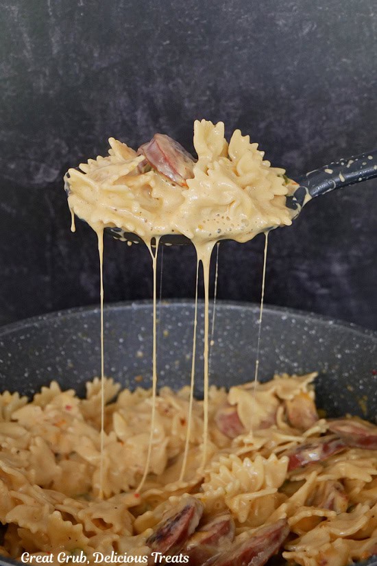 A big spoonful of cheesy smoked sausage bow tie pasta being scooped out of the pot.
