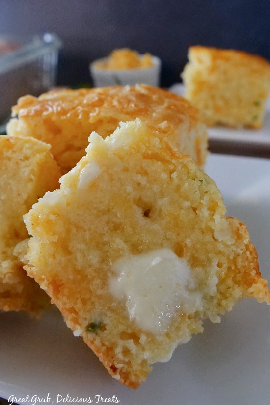 Cheesy Cornbread is a delicious cornbread recipe that makes for a great side or a filling snack. A piece of cornbread cut in half with melted butter on it.