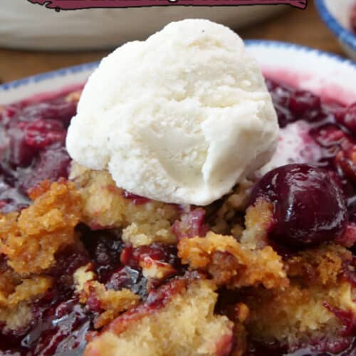 A white bowl with blue trim filled with a serving of cherry cobbler with a scoop of vanilla ice cream on top.