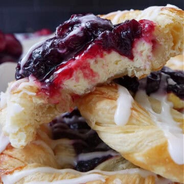A close up of three cherry pastries with a few bites taken out of the top pastry.