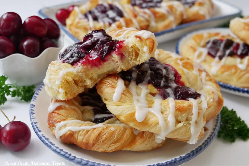 A horizontal photo of a white surface with white plates with blue trim filled with cherry cream cheese pastries.