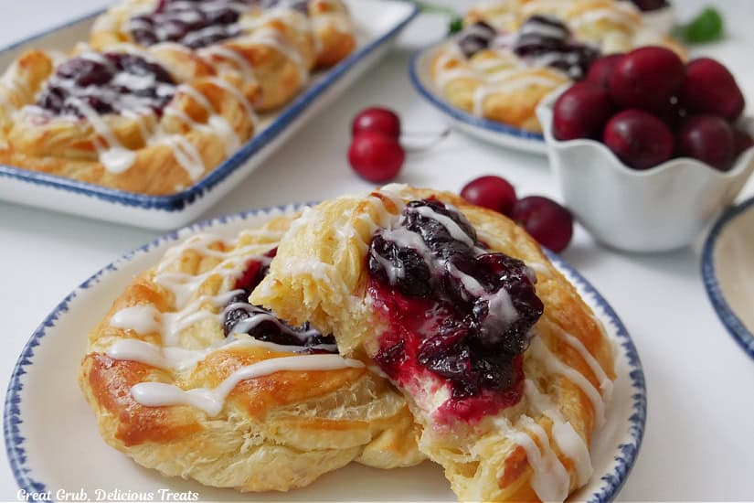White plates with two pastries on them with a small white bowl filled with cherries.