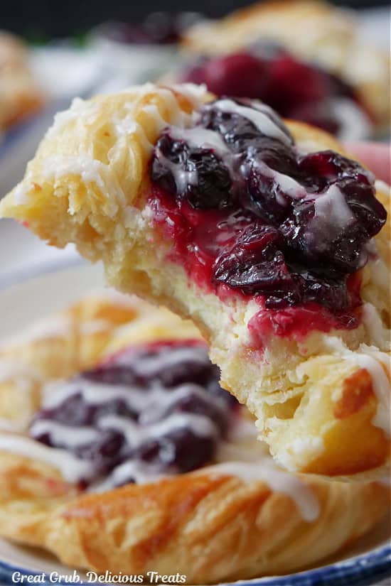 A close up of a cherry pastry held up to the camera lens with a few bites taken out of it showing the cheese and cherry filling.