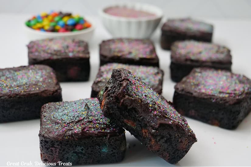 A white surface with nine chocolate brownies on it with a bite taken out of one of the brownies.