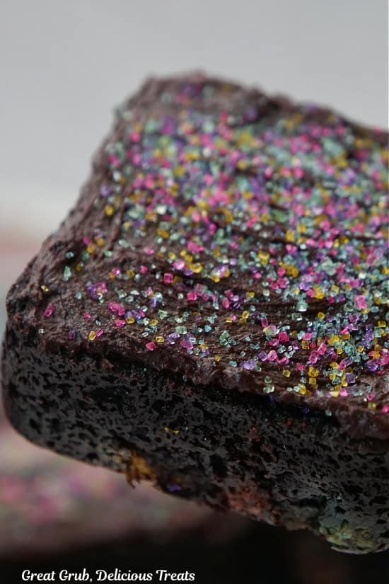A close up photo of a square frosted brownie with candy sprinkles on top.