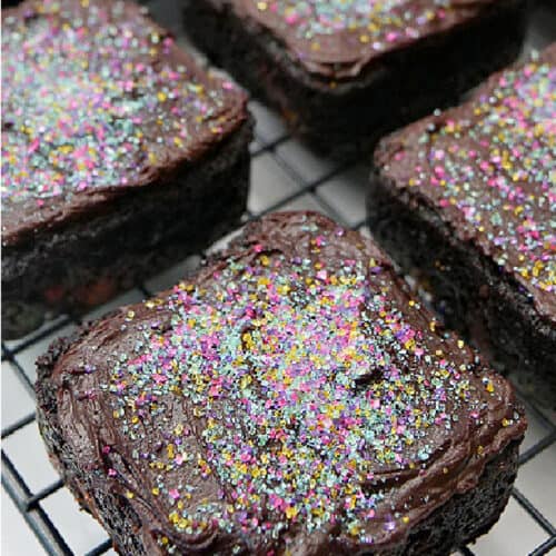 Square brownies on a wire rack with frosting and candy sprinkles on top.