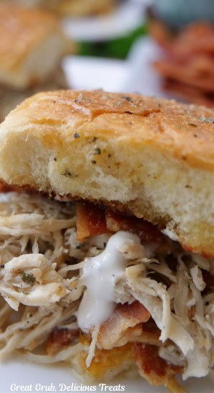 A close up of a slider with shredded chicken, bacon, cheese, and ranch dressing.