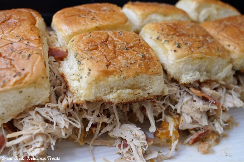 Eight shredded chicken sliders on a white plate.